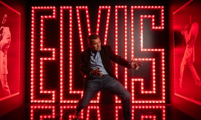 man poses in front of big elvis letters