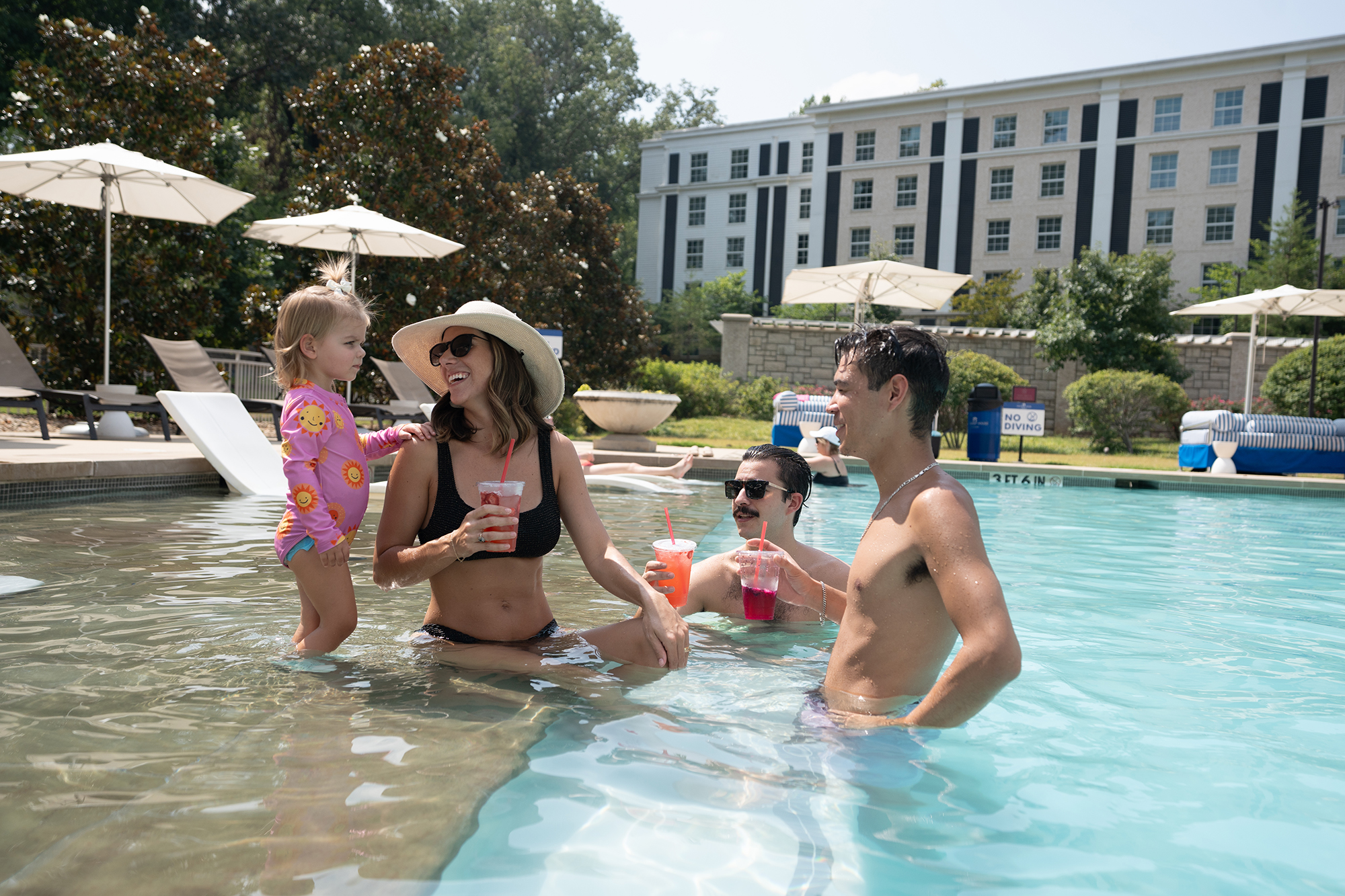 People lounging in the pool at The Guest House at Graceland. A woman and two men have drinks in their hands while the woman looks at a little girl next to her.