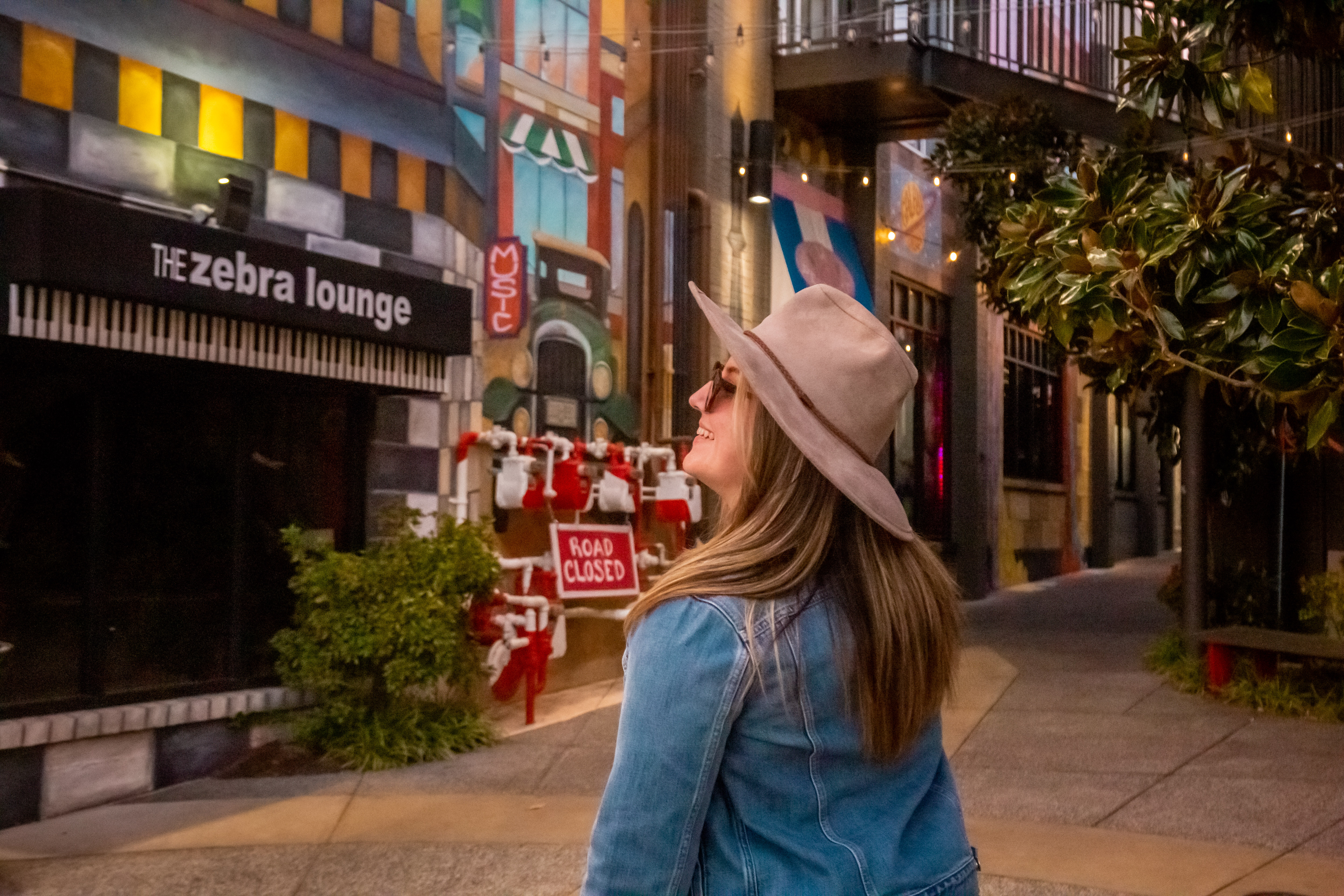 woman looks up smiling in front of shops and bars in overton square