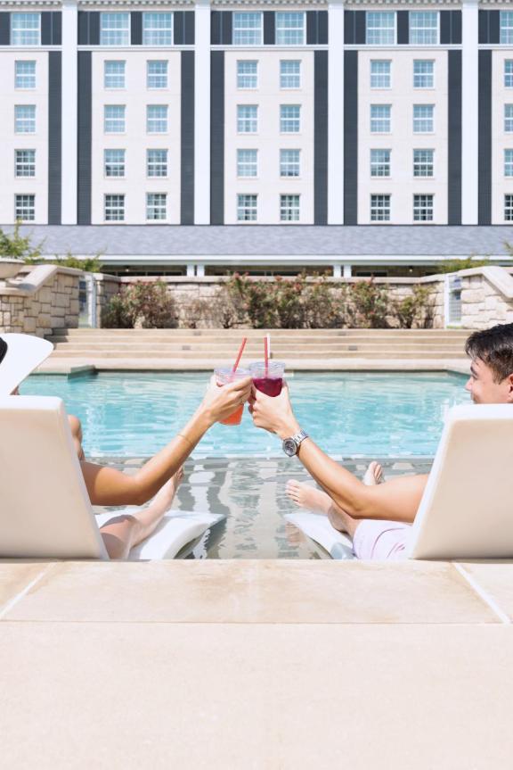 Couple tapping drink glasses together while lounging at the pool at Guesthouse at Graceland.