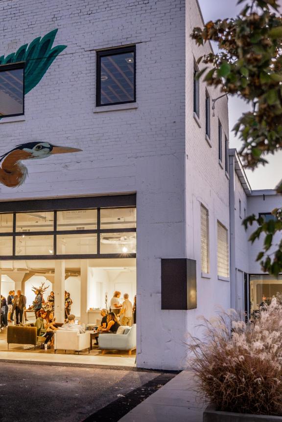 People inside the gallery space at Ugly Art Co with a large blueish-green bird mural above the entrance.