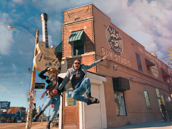 two people jump in the air in front of sun studio
