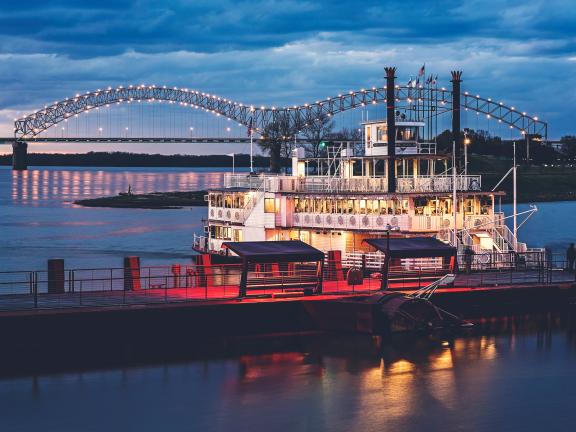 riverboat on Mississippi River with M bridge lit up in background