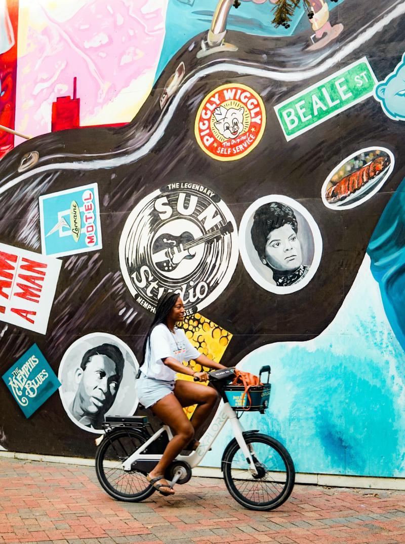 girl riding bike in front of mural