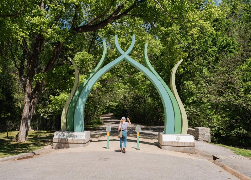 green sculptural gate entrance to old forest trail, woman walking through