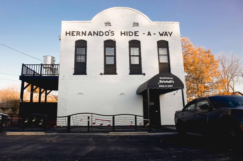 Exterior photo of Hernando's Hideaway Honky Tonk. The building is all white and two floors with the name above the windows