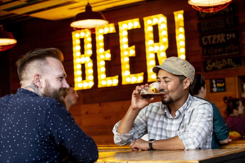 man drinks a beer at high cotton with neon beer! sign in background