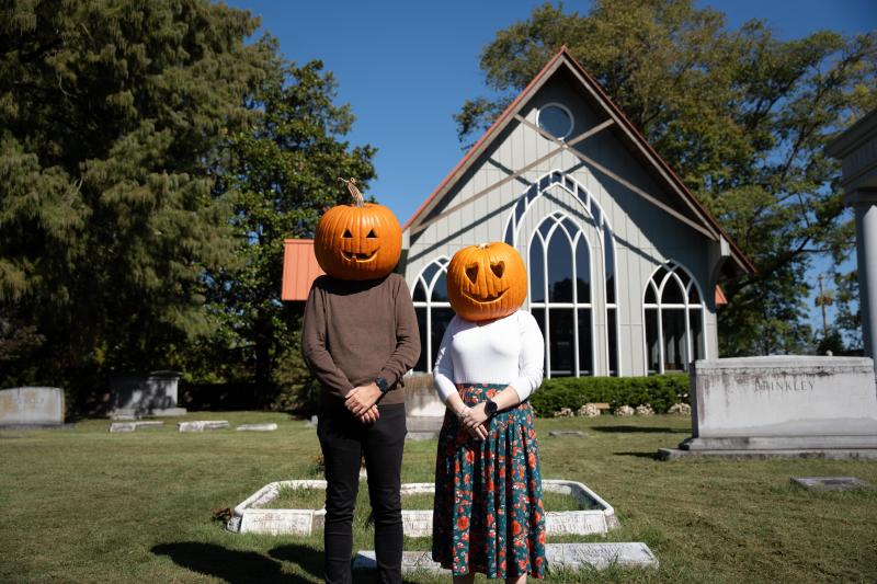 two people with pumpkin heads stand in front of chapel at elmwood cemetery