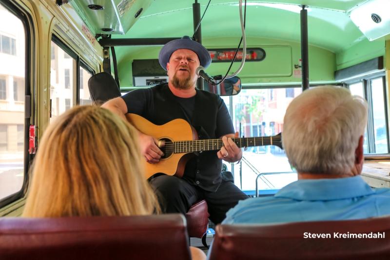 Tour guide singing with acoustic guitar on vintage bus