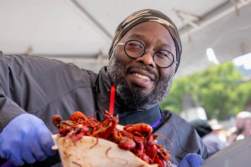 man holds up scoop of crawfish and smiles for photo