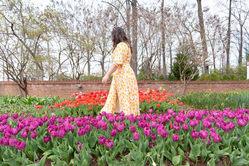 woman in flowy yellow dress walking through purple and orange flower field