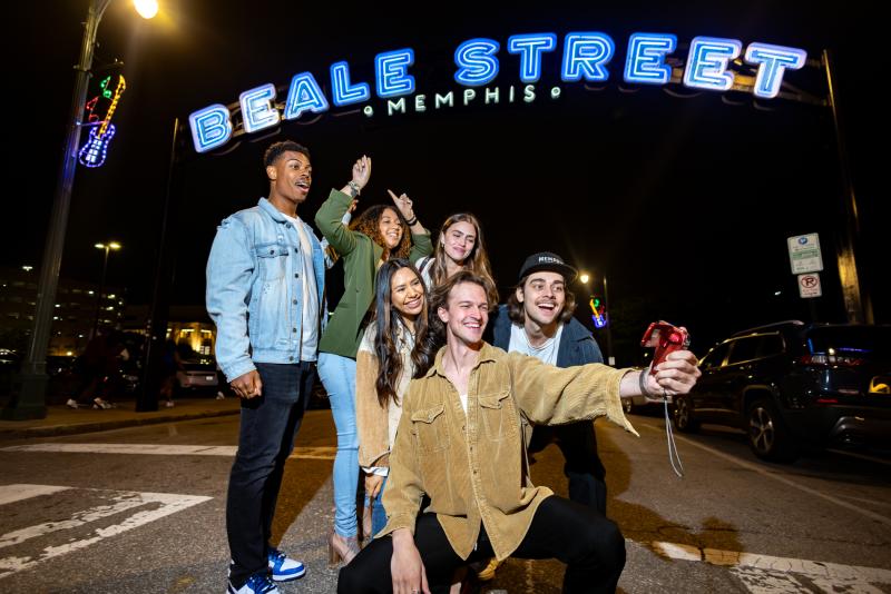 Friends pose for photo beneath the neon Beale Street sign.
