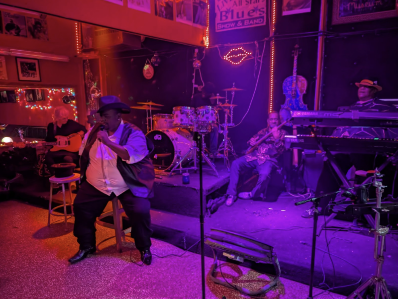 man wearing a cowboy hat singing on stage covered by red and purple lights