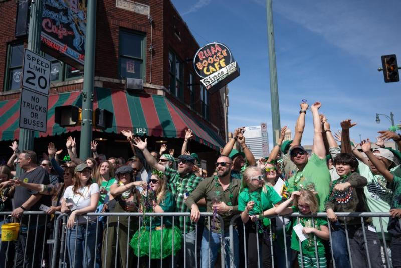 crowd of people dressed in green shirts and green beads all standing in a crowd with their hands up at the beale street parade
