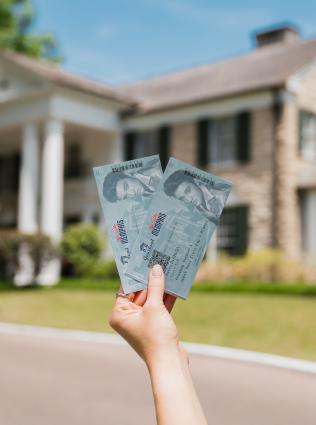 A visitor holding 2 tickets in front of Elvis Presley's Graceland Mansion
