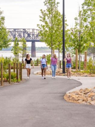A group of friends walks along a paved path lined with trees in Memphis' Tom Lee Park