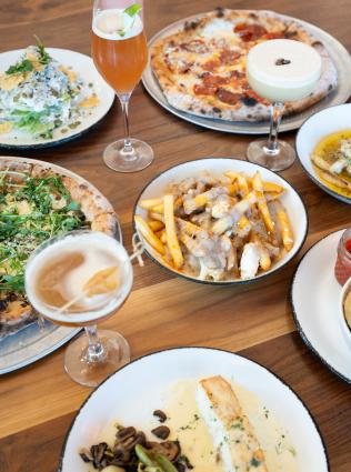 several plates of food from hog and hominy like pizzas and fries