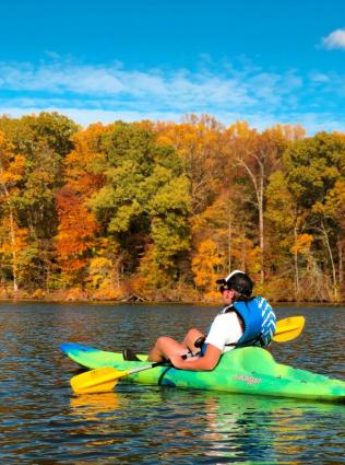 man kayaks on lake during fall with leaves changing