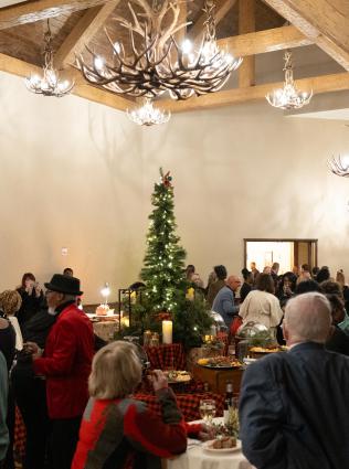 Crowd of members mingling around cocktail tables and talking in Big Cypress Lodge Gallery at 2024 holiday party with Christmas tree in the background, photo by Julian Harper