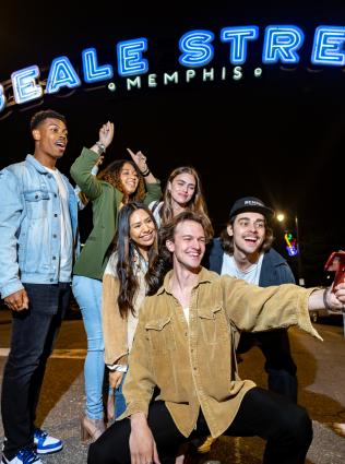 Friends posing for a selfie under the neon blue Beale Street sign.
