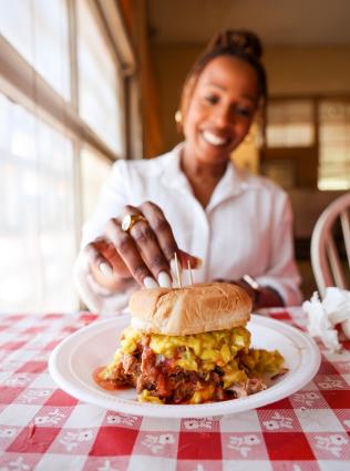 woman reaches for pulled pork sandwich