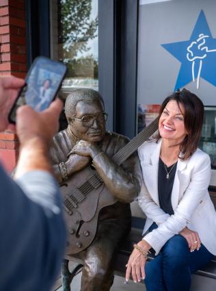 Woman posing with the Little Milton statue outside the Blues Hall of Fame