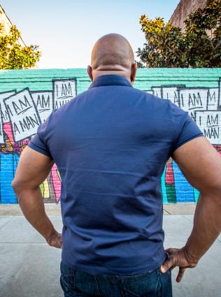 A man standing in front of the I AM A MAN mural on South Main representing the Memphis Sanitation Strike of 1968.