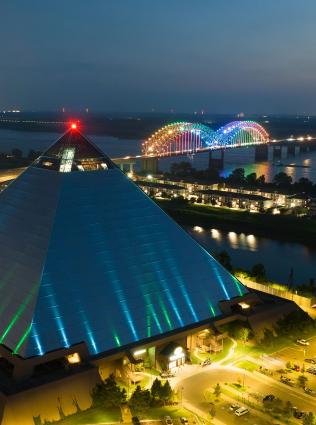 Aerial view of Bass Pro Shops at the Pyramid and the Mighty Lights aglow on the Hernando de Soto bridge over the Mississippi River at night.