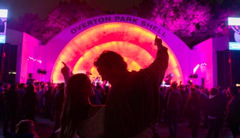 Couple listens to a concert at Overton Park Shell, which is illuminated in pink and orange neon lights.