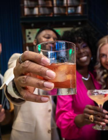 four friends hold up cocktails and smile for photo