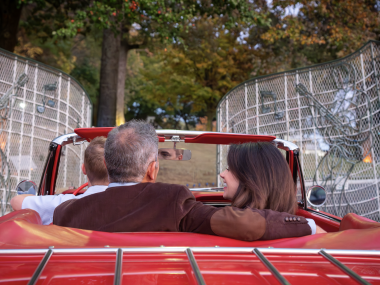 couple sits in red convertible driving through graceland gates