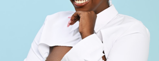African American Woman with Blonde Buzed Hair, pink bow, smiling into the camera against a light blue background