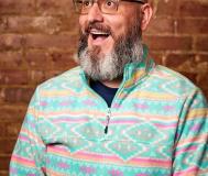 white man with very full beard and glasses smiling and looking up in front of a brick wall (picture is only from the neck up)