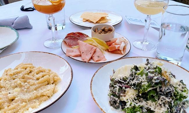 plates of pasta, salad, charcuterie, and cocktails on a white tablecloth on a patio