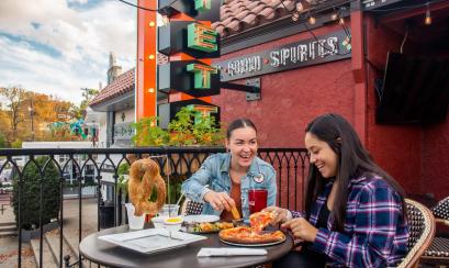 two ladies outside on the patio laughing while eating a soft pretzel and pizza