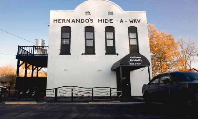 Exterior photo of Hernando's Hideaway Honky Tonk. The building is all white and two floors with the name above the windows