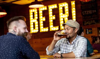 man drinks a beer at high cotton with neon beer! sign in background