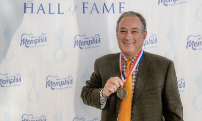 man stands posing with medal in front of step and repeat