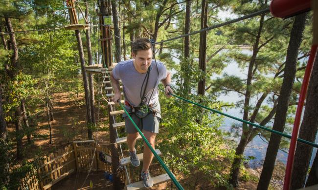 man climbs across treetop bridge
