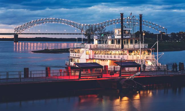Riverboat on Mississippi River with the Hernando de Soto bridge lit up in the background.