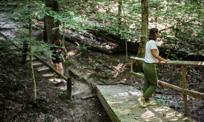 woman stands on trail bridge in forest