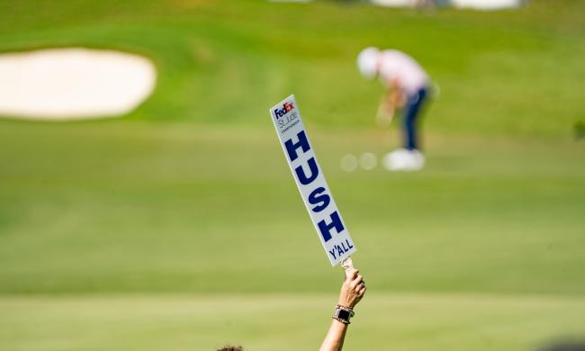 volunteer holds up hush y'all sign with golfer blurred in background
