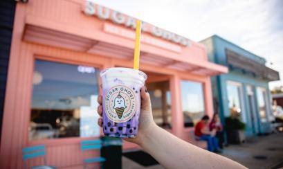 bubble tea held up in front of pink sugar ghost building
