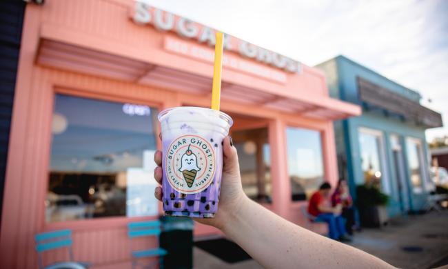 Bubble tea held up in front of pink Sugar Ghost building