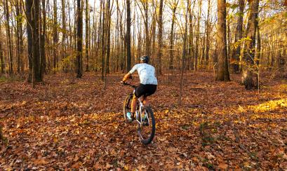 man rides bike through Stanky Creek Cycling path covered in leaves in the fall