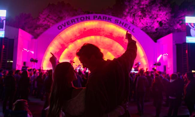 Couple listens to a concert at Overton Park Shell, which is illuminated in pink and orange neon lights.