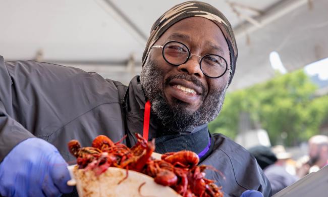 man holds up scoop of crawfish and smiles for photo
