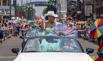 Person waves from convertible vehicle during Pride parade