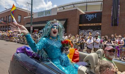 drag queen participant waves from convertible in pride parade