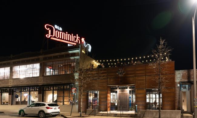 Exterior of Old Dominick Distillery at night with the red and white neon sign illuminated.